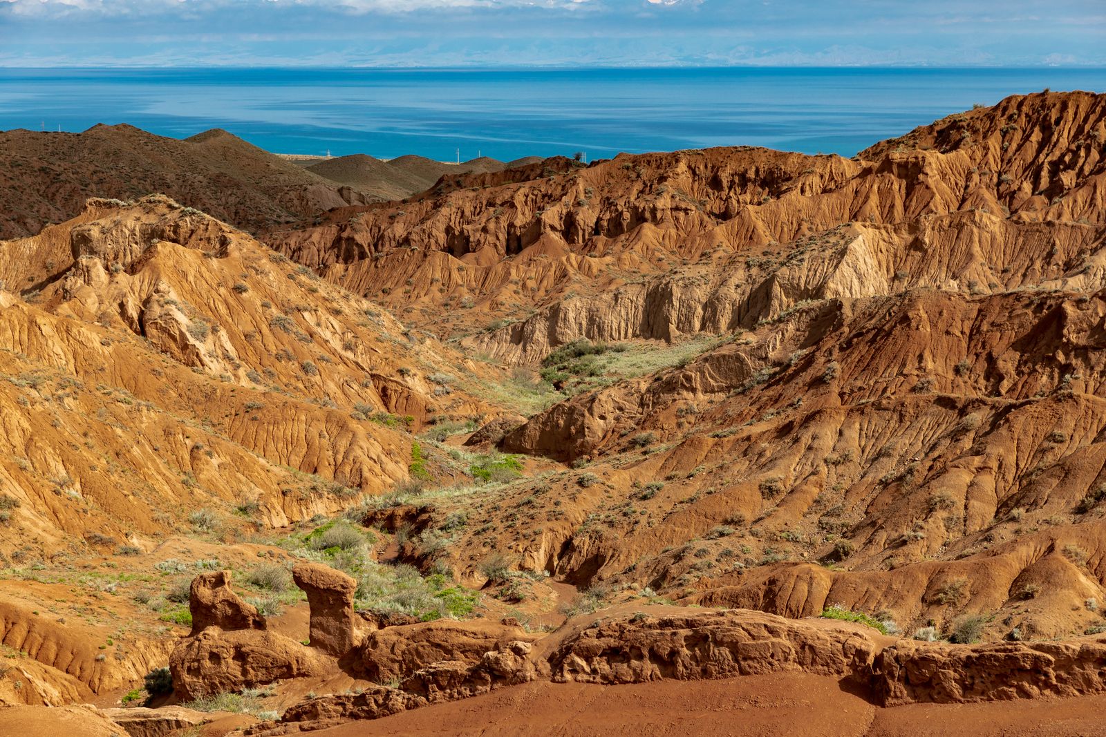 Red and yellow eroded ridges of Skazka canyon, with Issyk-Kul behind